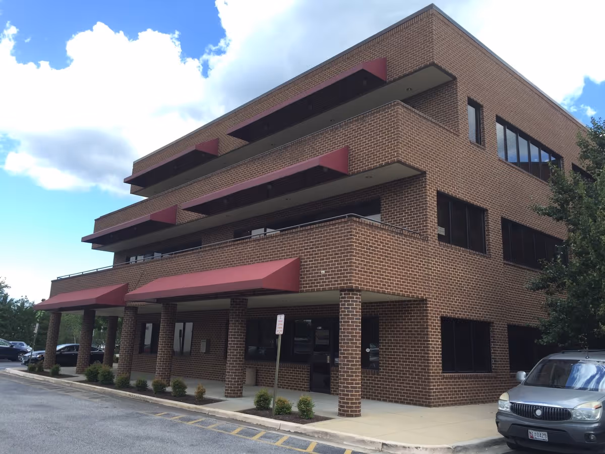 Brick multi-story nursing facility exterior with red awnings and front entrance.