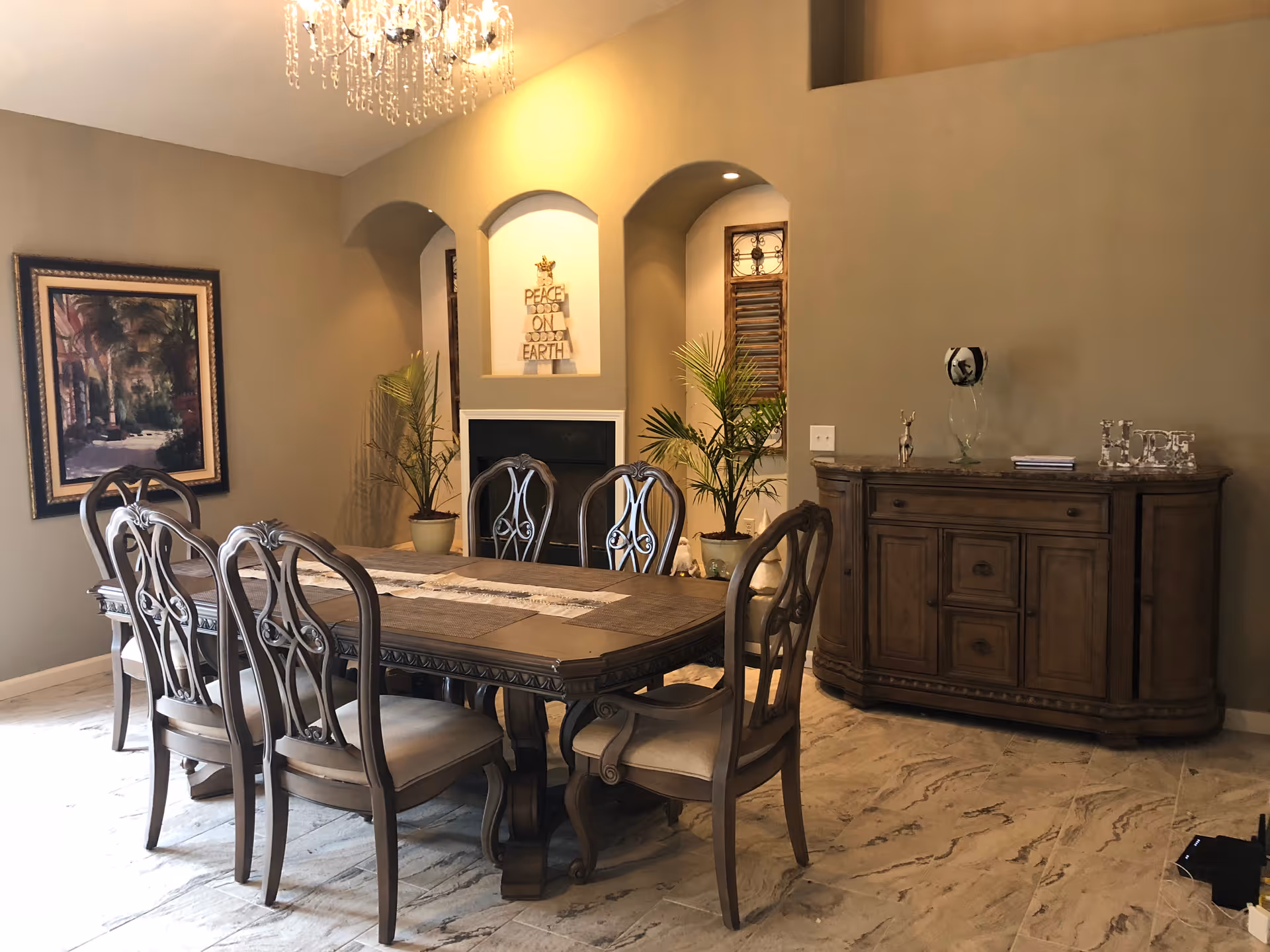 Elegant dining room with a wooden table and chairs, chandelier, sideboard, decorative plants, and framed artwork.