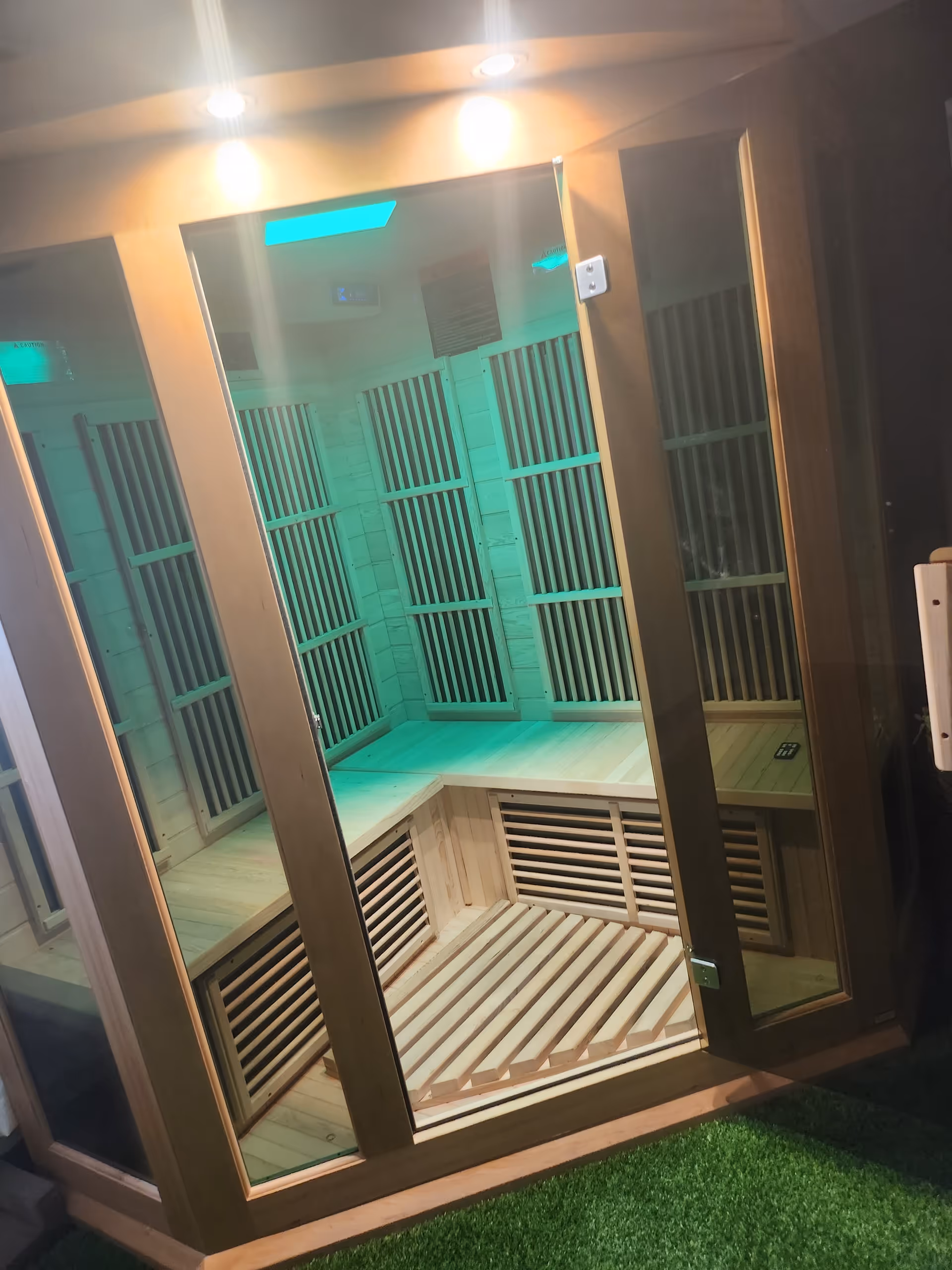 Glass-fronted sauna with wooden benches and green lighting inside.