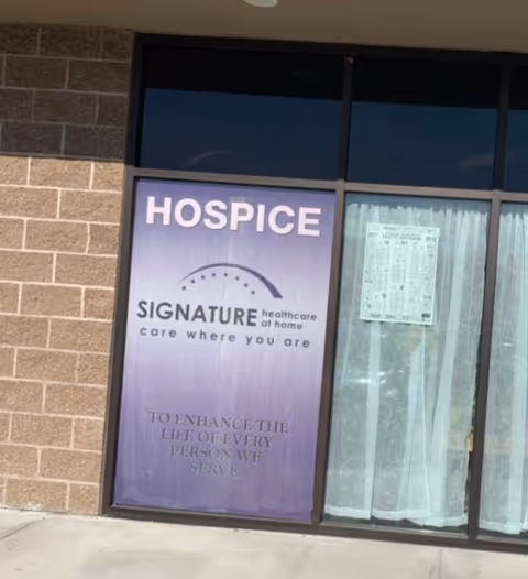 Exterior storefront with a purple Hospice SIGNATURE sign on brick wall.