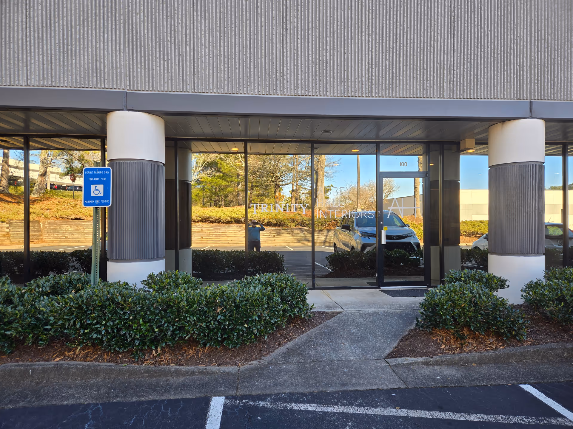 Glass entrance to Trinity Life At Home with parking lot and shrubs.