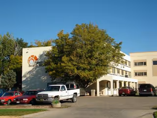 Exterior view of Courtyard Care Center with parked cars, trees, and a light-colored façade.