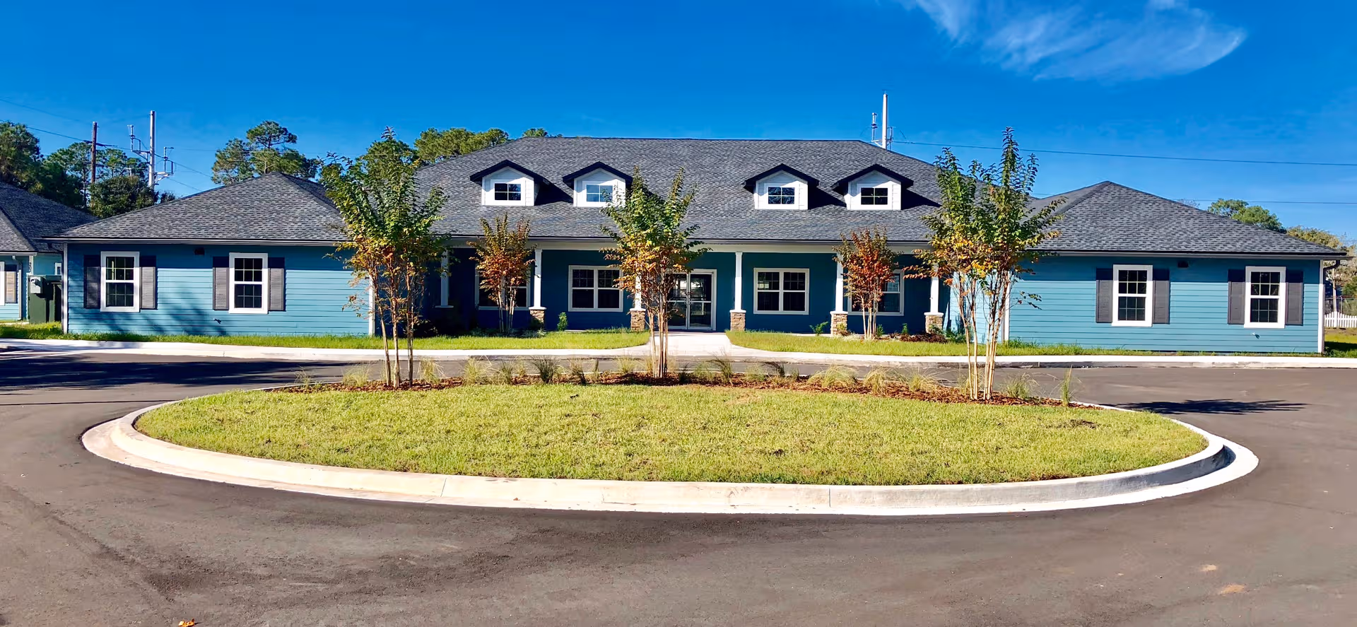 Blue single-story senior living facility with a circular driveway and greenery.