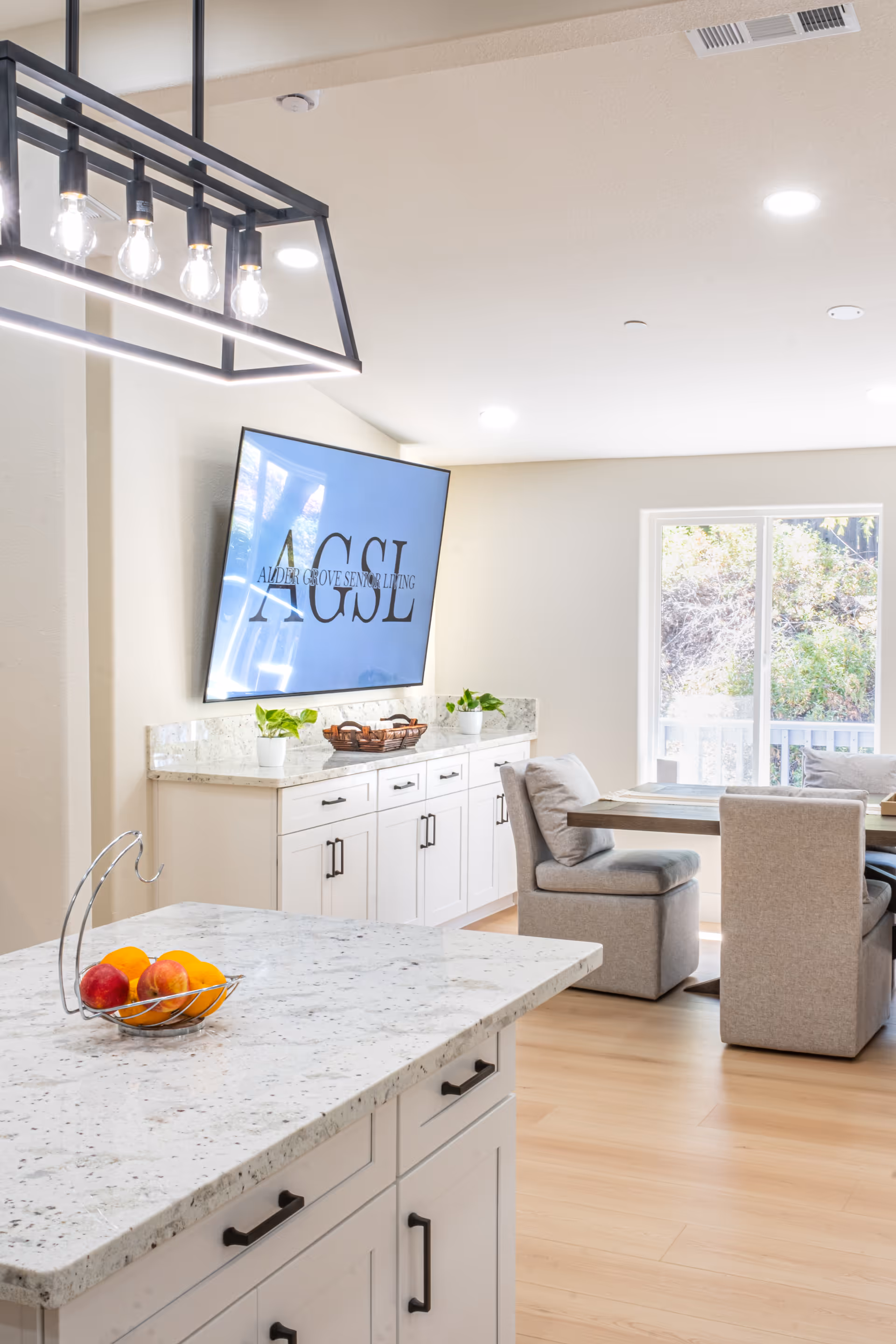 Open-concept kitchen and dining area with white cabinets, granite counters, and a wall-mounted TV.