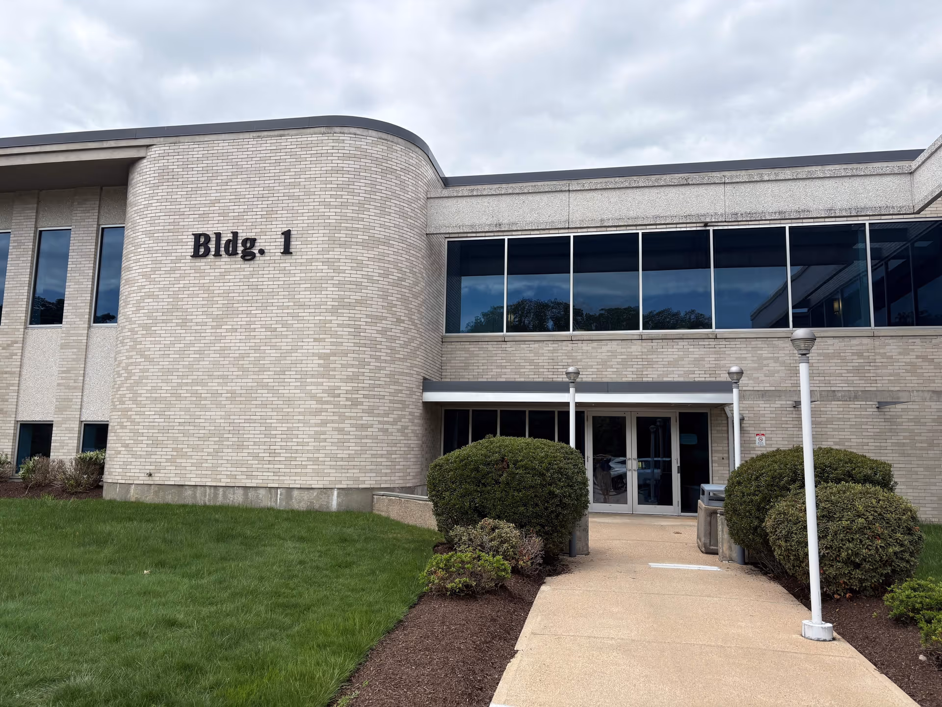 Front view of a brick building labeled Bldg. 1 with glass windows and a walkway.