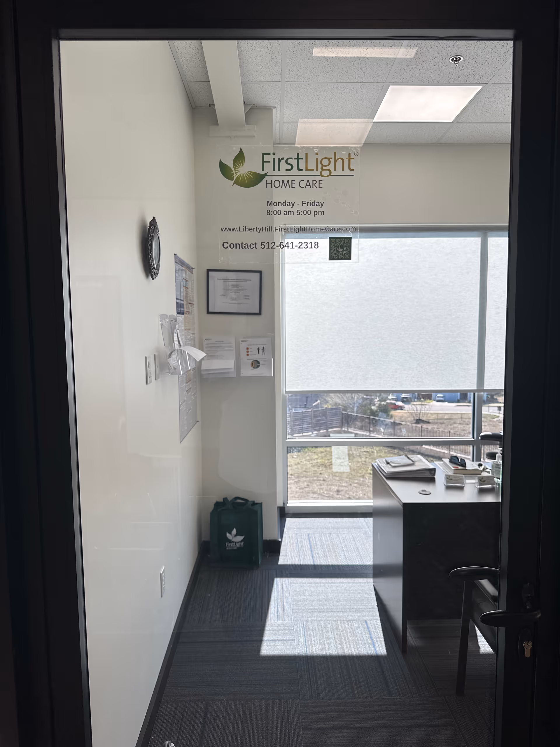 Office interior behind glass door with FirstLight Home Care sign and desk.