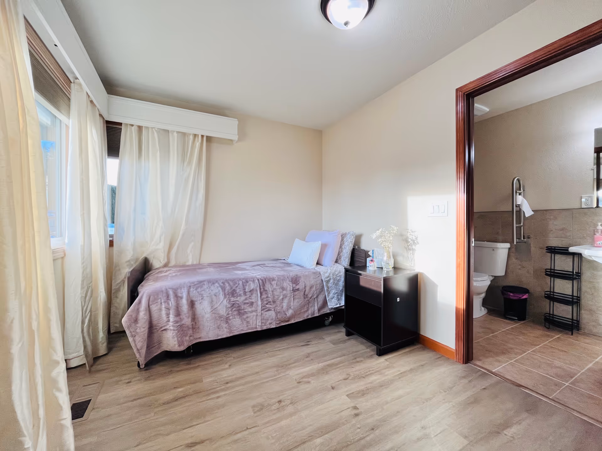 Bedroom in Serene Haven Senior Cares LLC facility with a bed, nightstand, and adjacent bathroom.