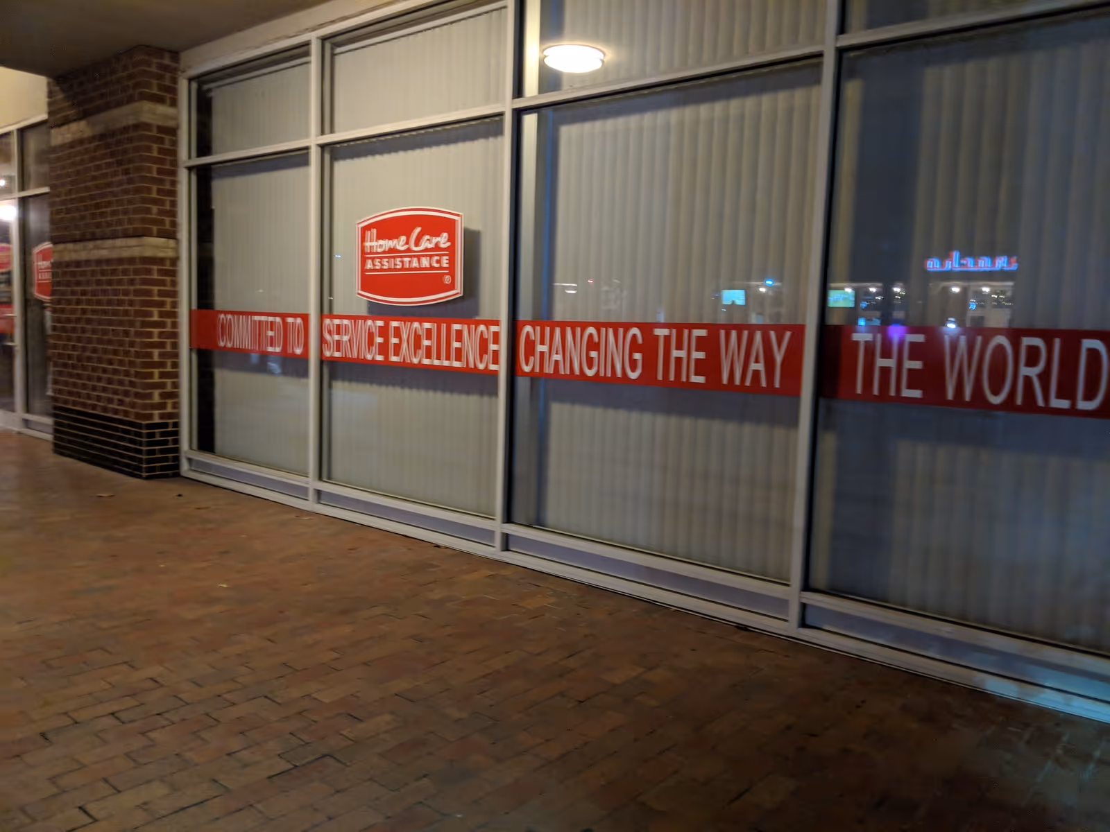 Exterior of Home Care Assistance storefront with red banners across glass windows at night.