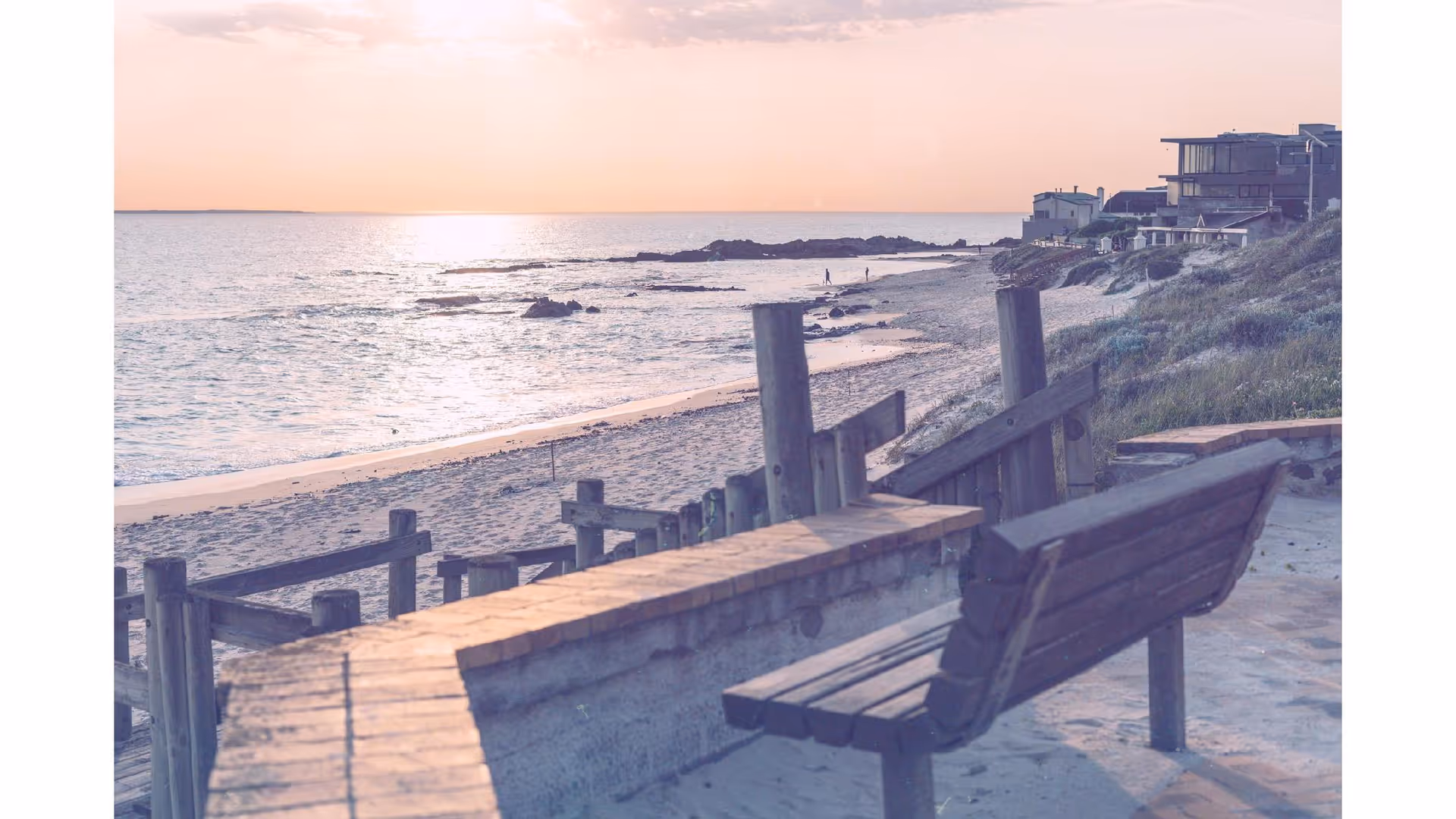 Beach at sunset with a wooden bench and weathered boardwalk railing.
