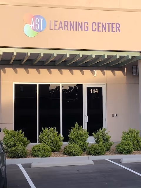 Exterior storefront with glass doors, small shrubs, and a parking lot in front.