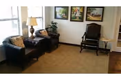 Cozy senior living lounge with two armchairs, a lamp, and framed artwork.