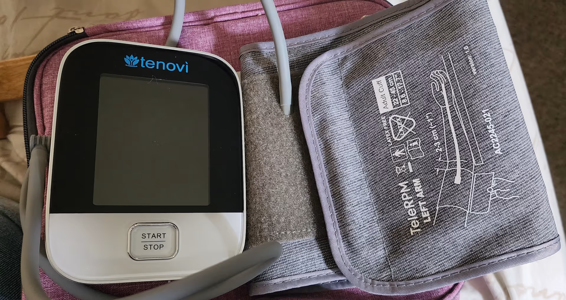 Close-up of a Tenovi blood pressure monitor and cuff resting on a pink surface.