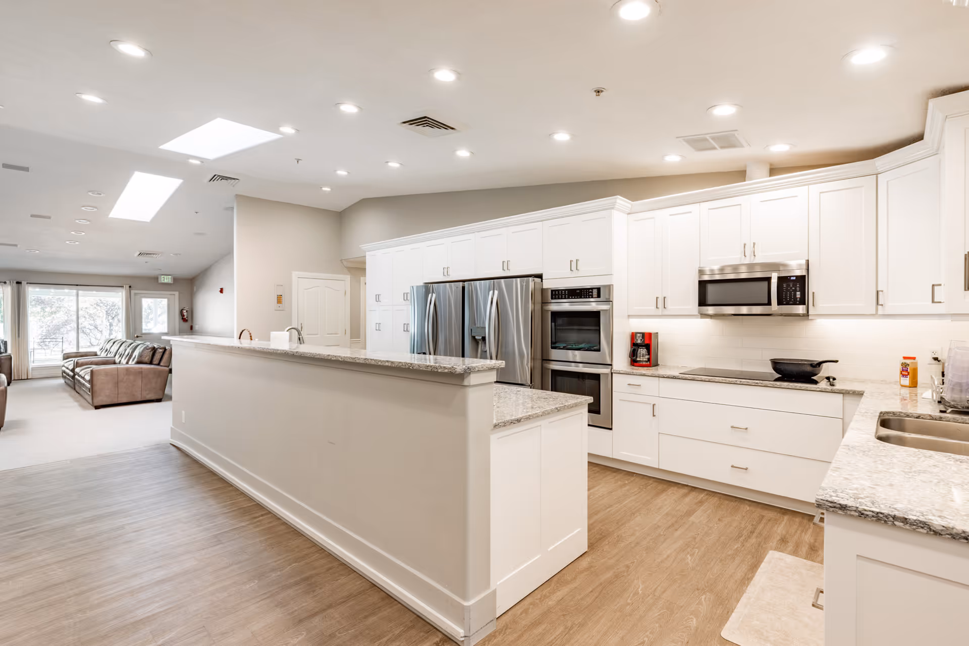 Bright white kitchen with granite countertops and stainless steel appliances beside a lounge area.