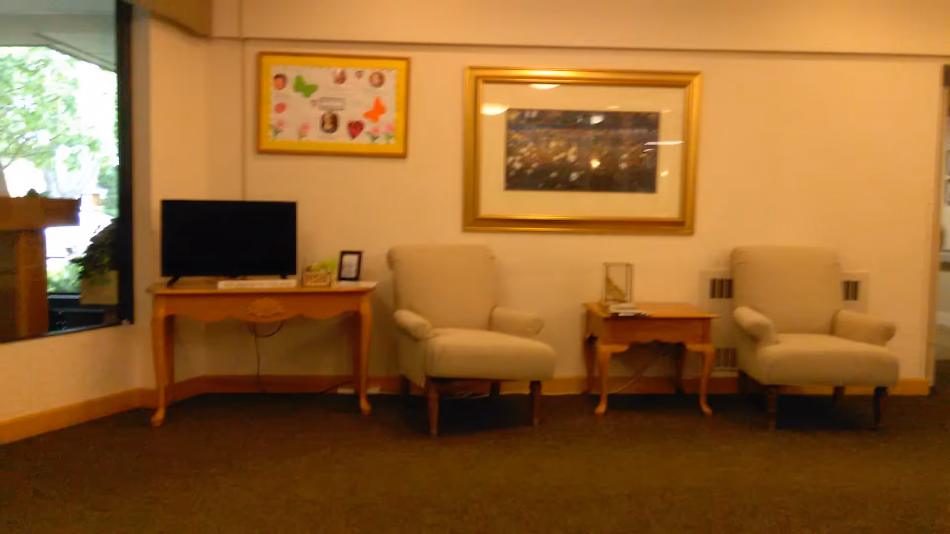 Interior lounge at Haven Homes Assisted Living with two cream chairs, tables, and TV.