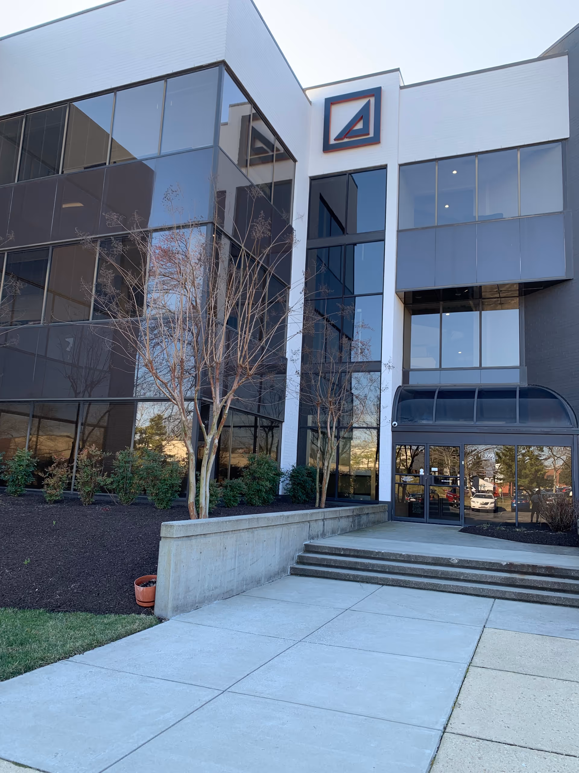 Modern glass-front building exterior with a glass entrance and concrete steps.