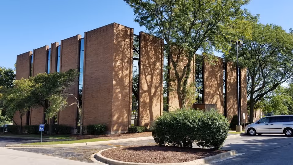 Exterior brick facility with tall windows, trees, and a minivan in the parking lot.