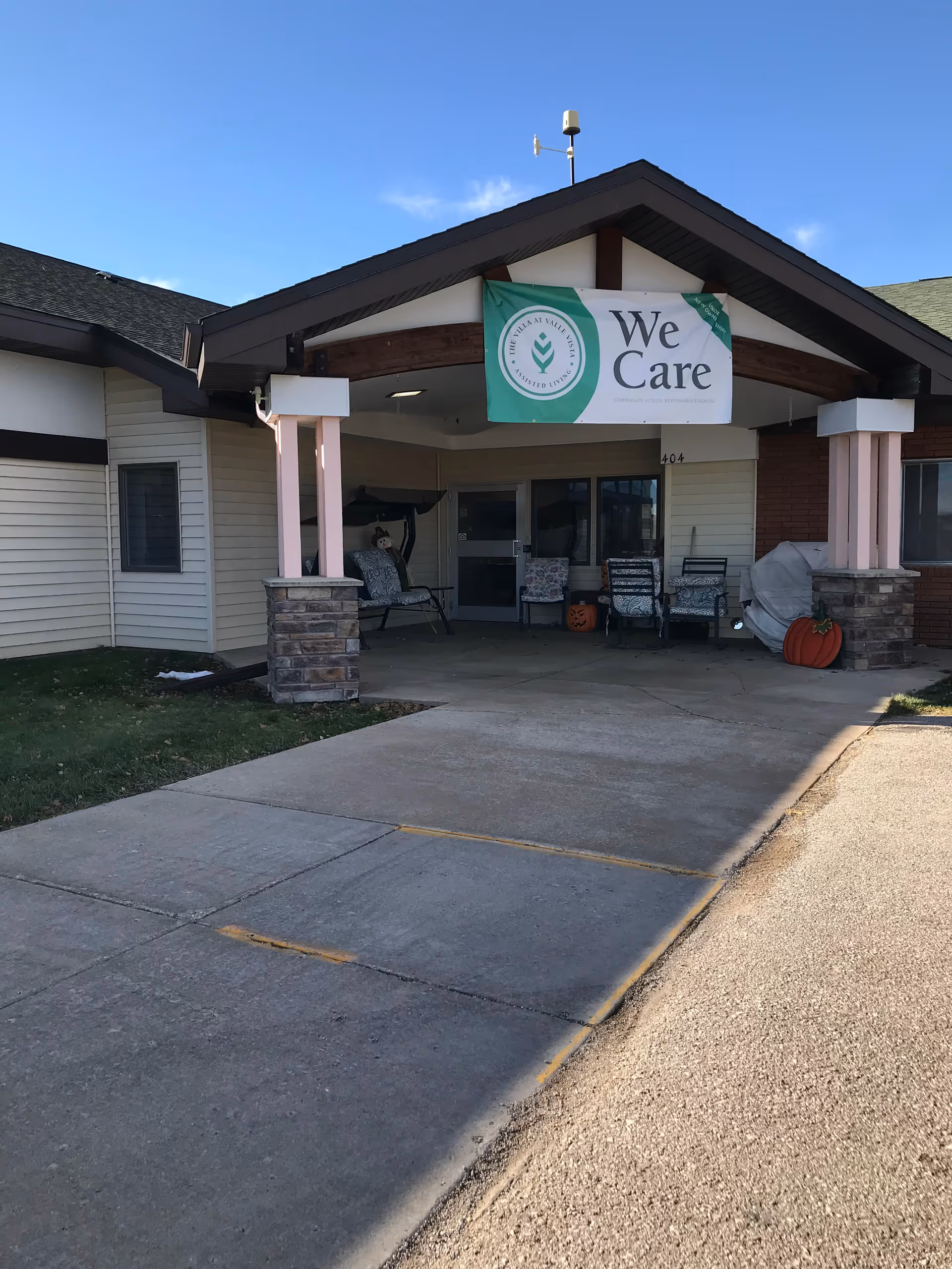 Front entrance of The Villa senior living facility with chairs, pumpkins, and a We Care banner.