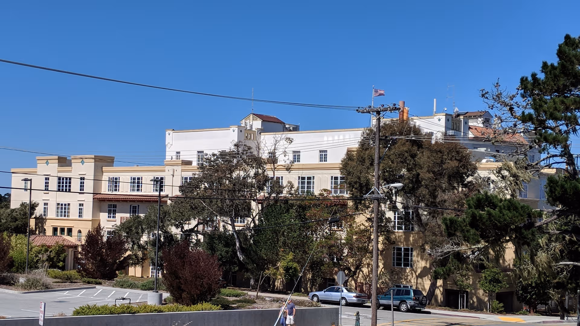 Exterior view of beige senior living facility with trees and parked cars under a blue sky.