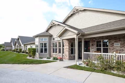 Exterior view of a senior living facility with brick facade, porch, and landscaped walkway.