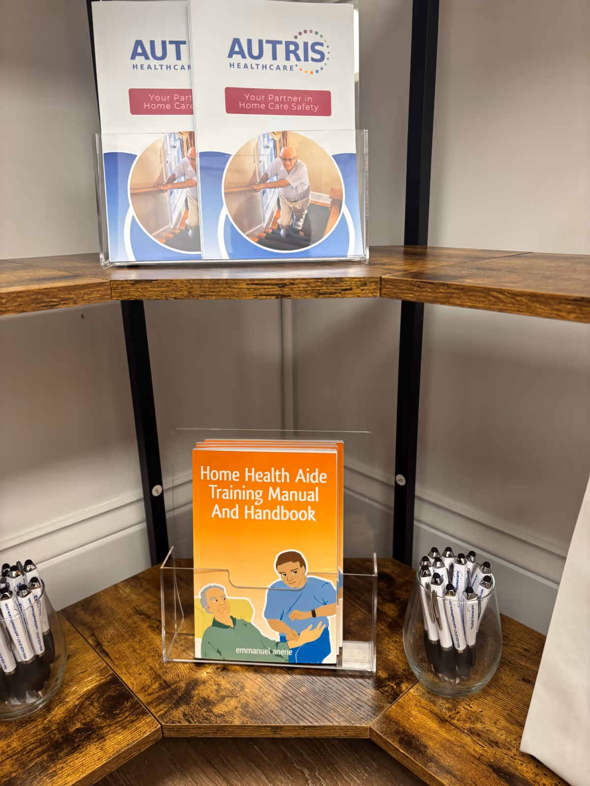 Display shelf with Autris Healthcare brochures and an orange Home Health Aide Training manual, plus pens.