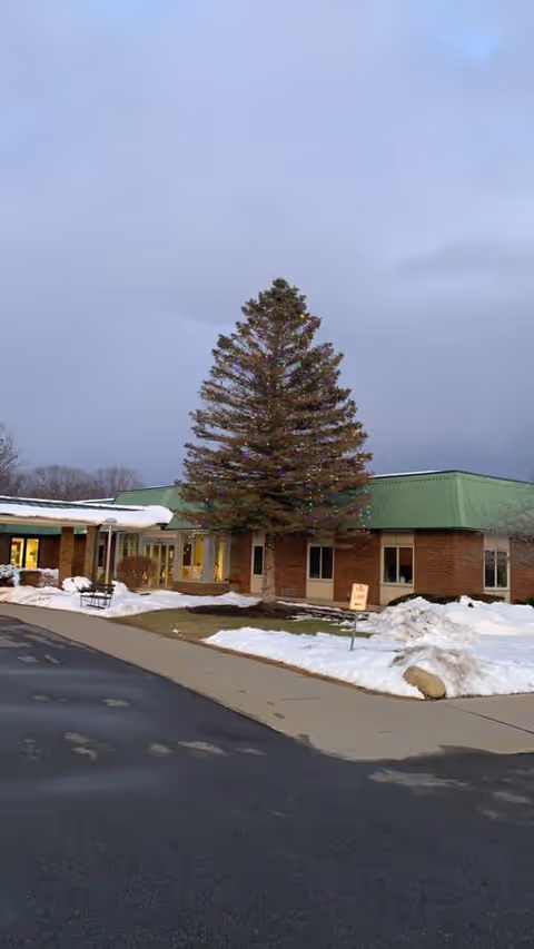 Exterior view of River Ridge Living Center with a tall tree, brick walls, and snow.
