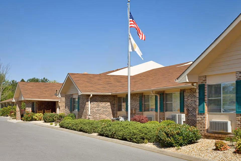 Single-story brick senior living center with flagpole and manicured shrubbery.