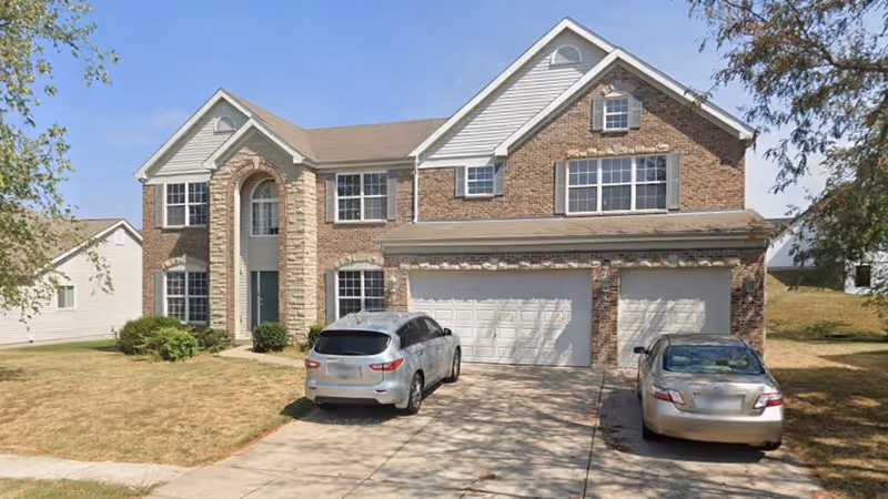 Two-car brick house with a front entrance and two parked cars in the driveway.