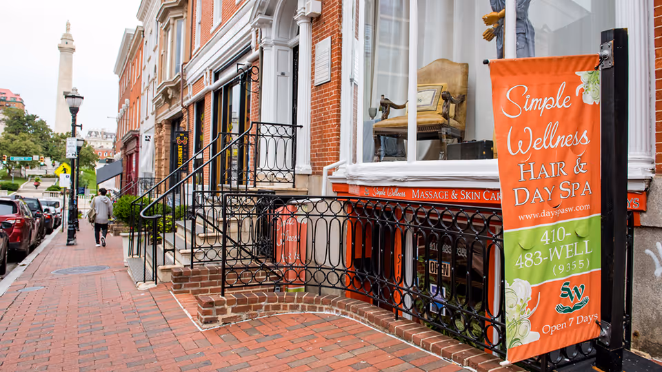 Brick sidewalk with storefronts and ornate railing, featuring an orange Simple Wellness banner.