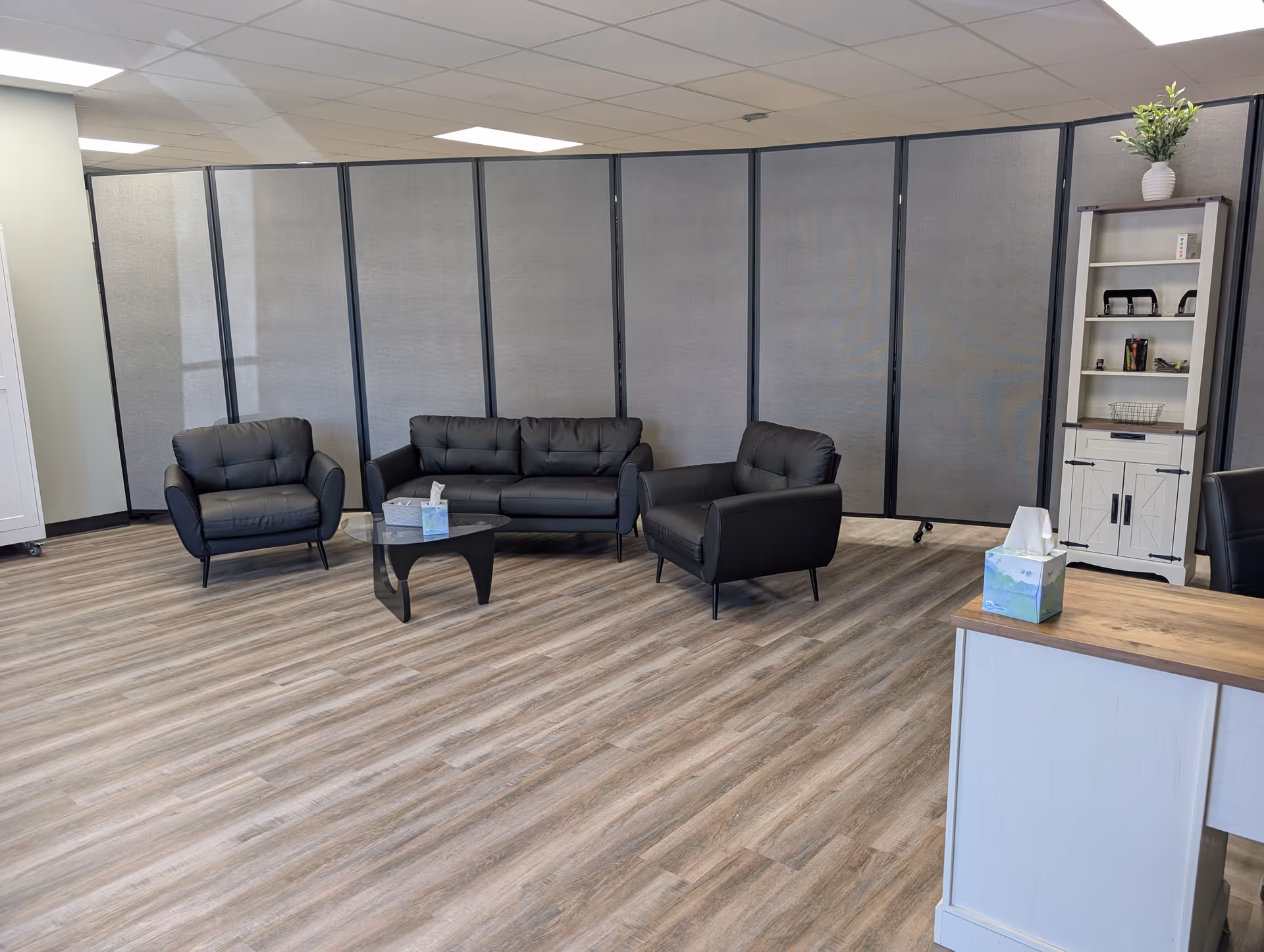 Modern lounge area with black leather chairs, partition screens, and a small reception desk.