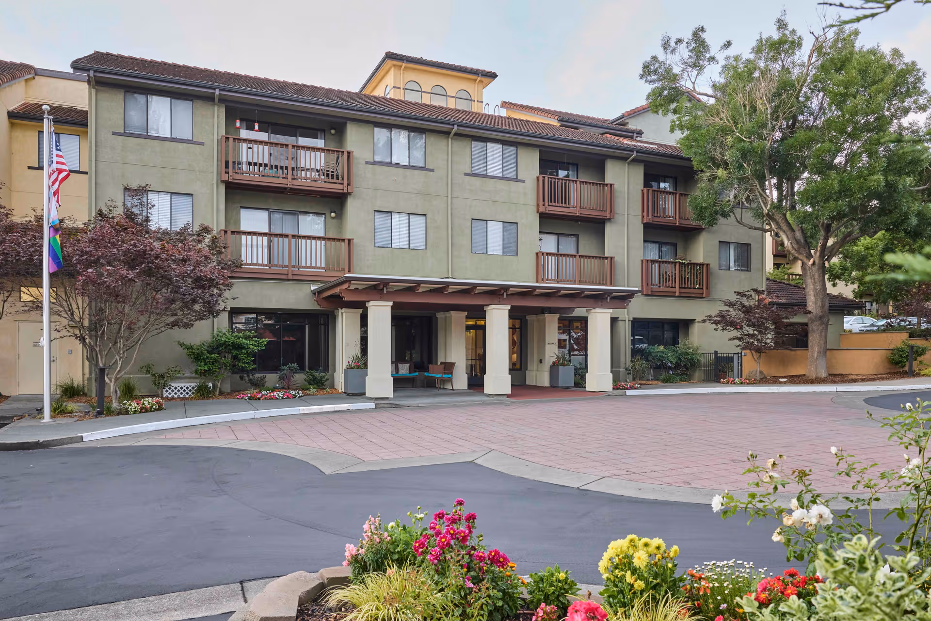 Drake Terrace senior living building with balconies, entrance canopy, flag, and landscaped foreground