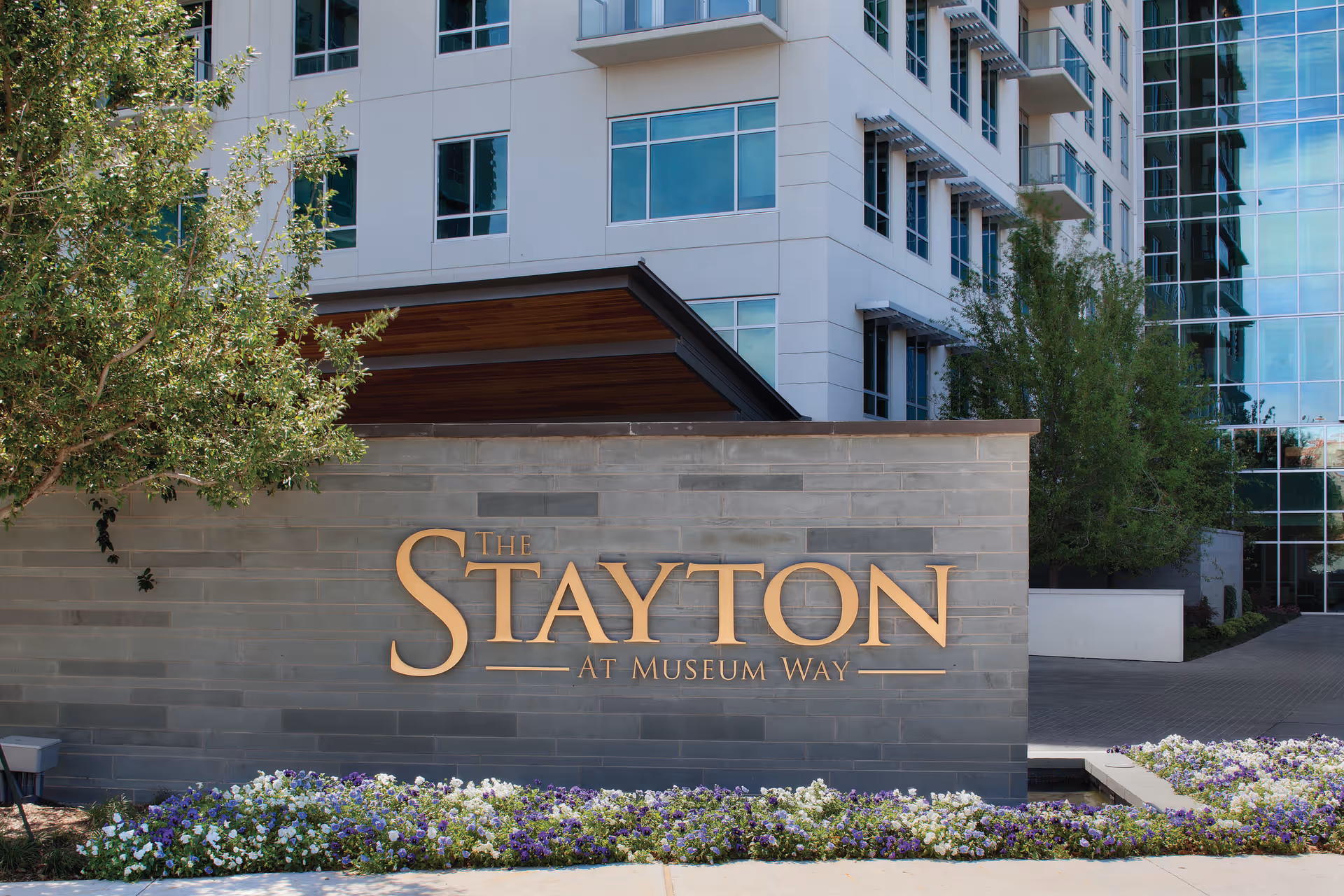 Front view of The Stayton at Museum Way sign beside a glass modern building.