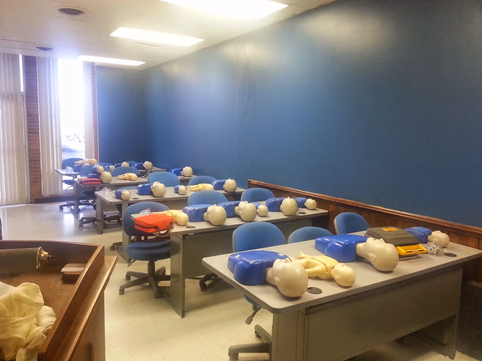 Interior training room with multiple CPR mannequins on desks and blue chairs.