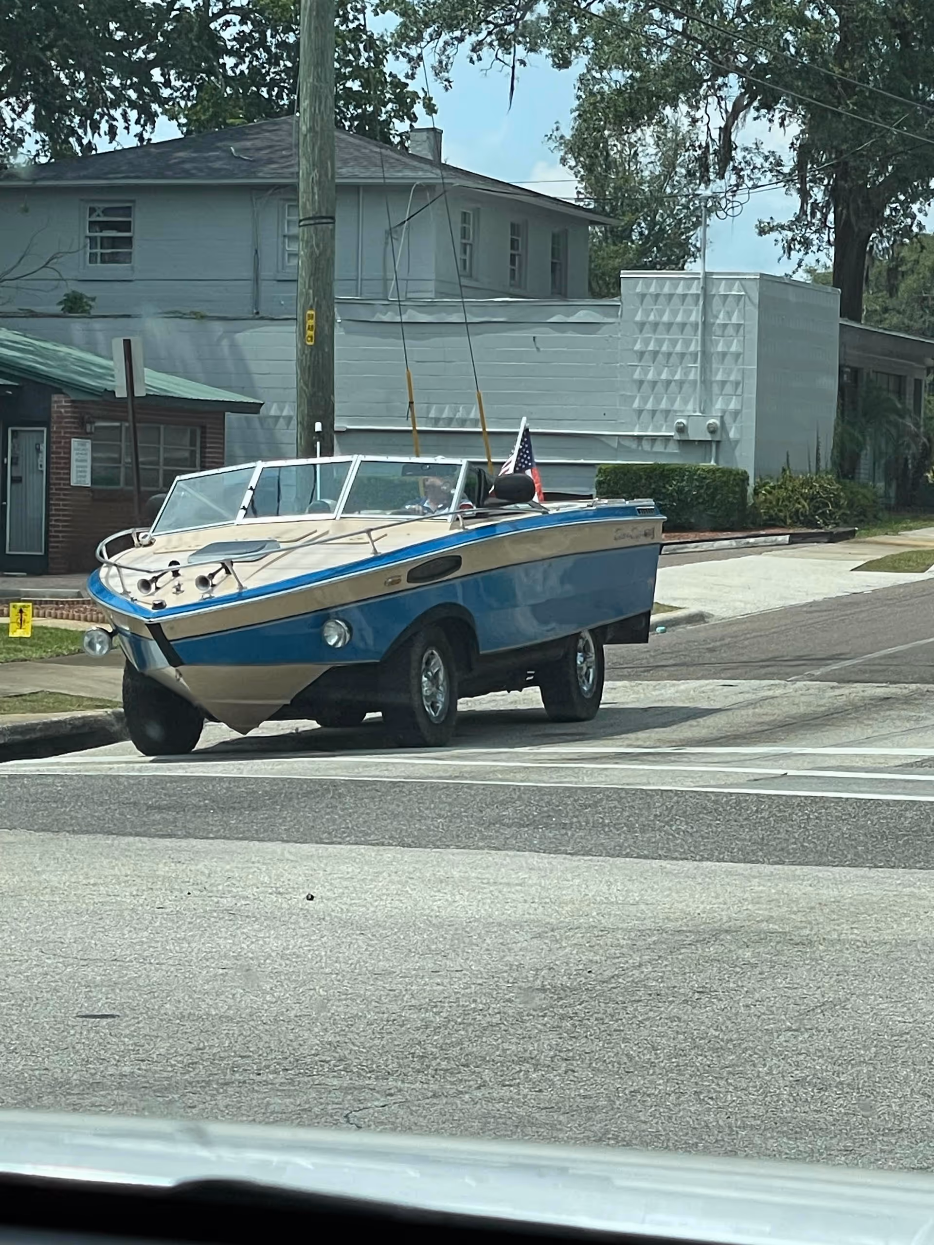 Blue motorboat on a trailer parked on a residential street with houses behind.