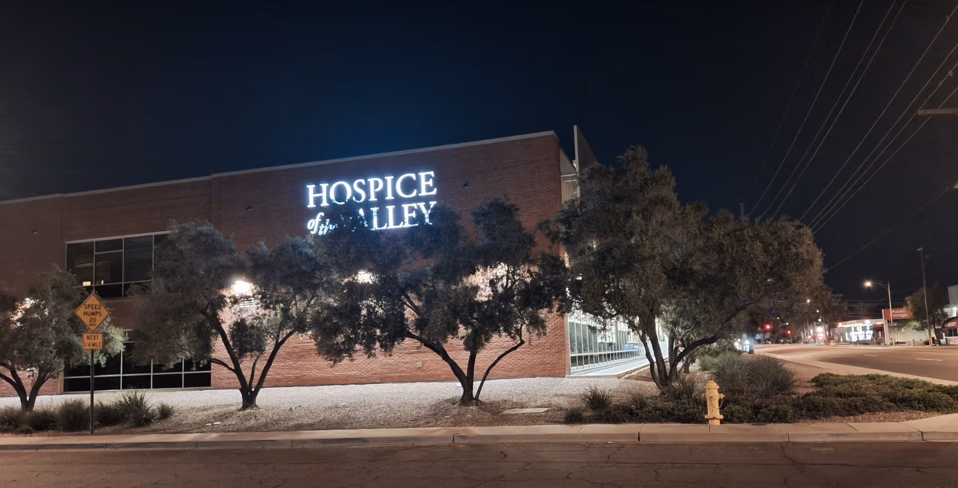 Night exterior of Hospice of the Valley building with trees and streetlights.