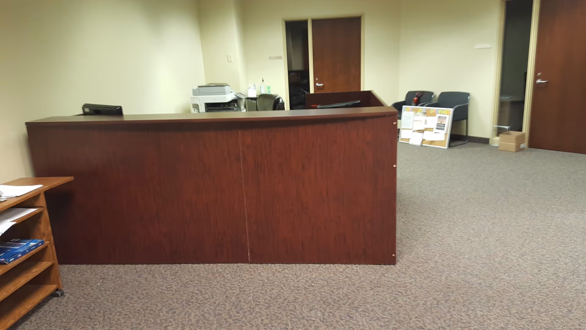 Dark wood reception desk dominates an empty lobby with chairs and doors in back.