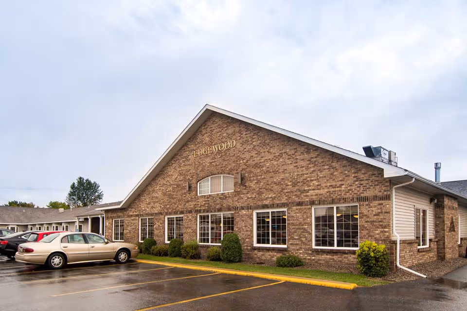 Brick senior living center exterior with large windows, shrubs, and a parking lot.