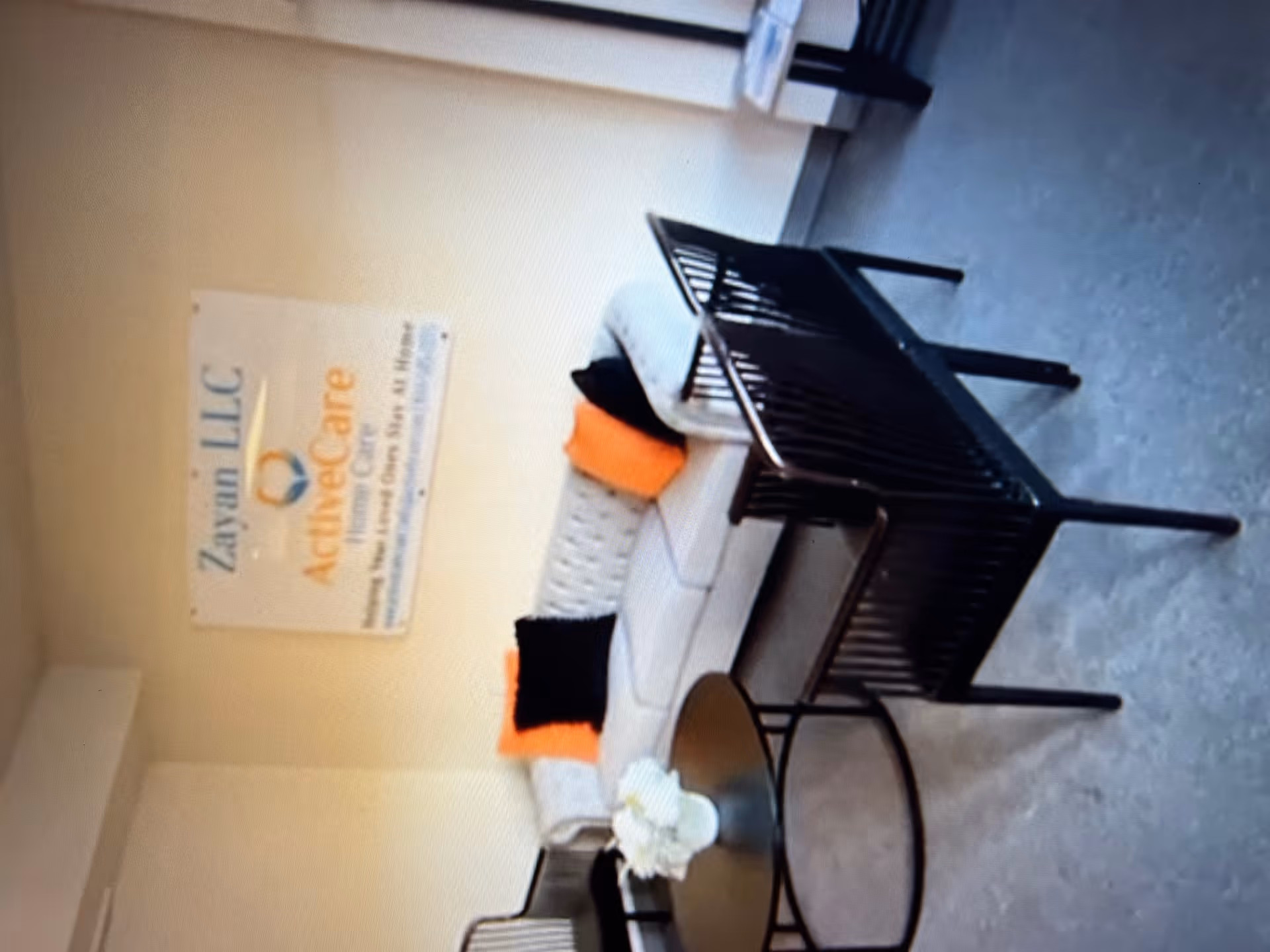 Interior lounge area with couch, orange cushions, black chairs, round table, and a sign on wall.