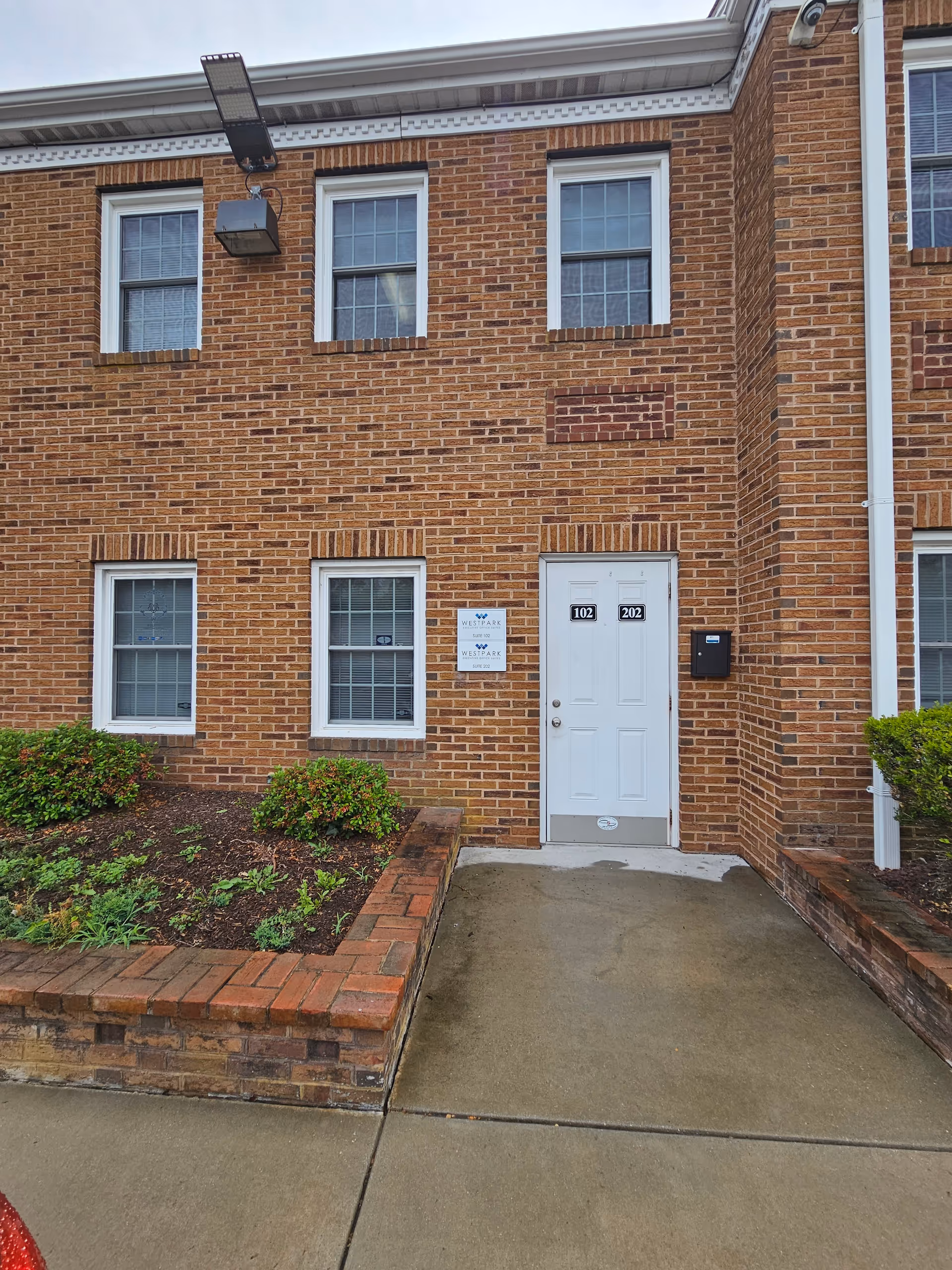 Brick exterior of a senior living building with a white door labeled 102 and 202.