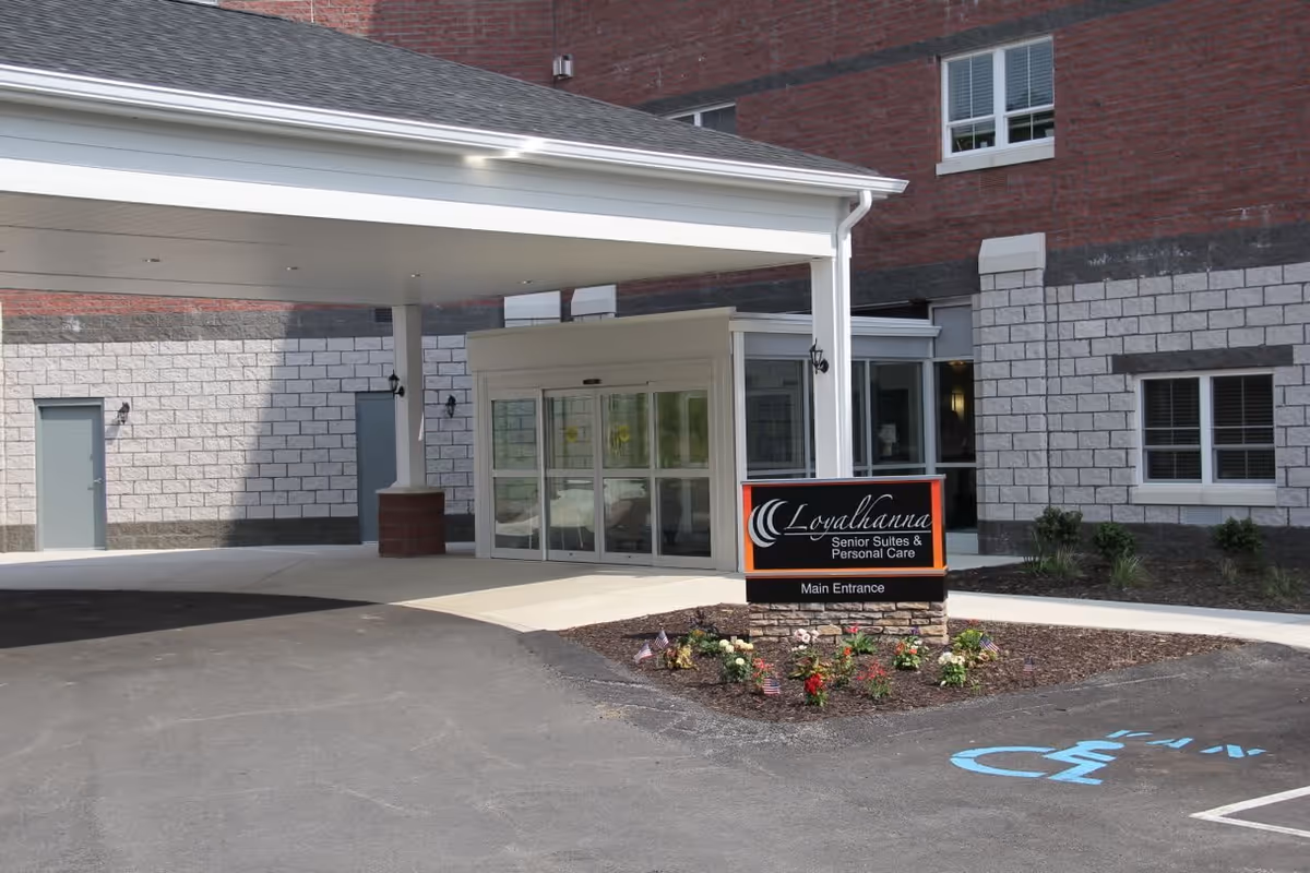 Covered main entrance of Loyalhanna Senior Suites and Personal Care with an entry canopy, glass doors, a planted sign, and a marked handicap parking space.