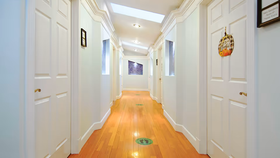 A bright, long corridor with white doors and light blue walls in a senior living facility.
