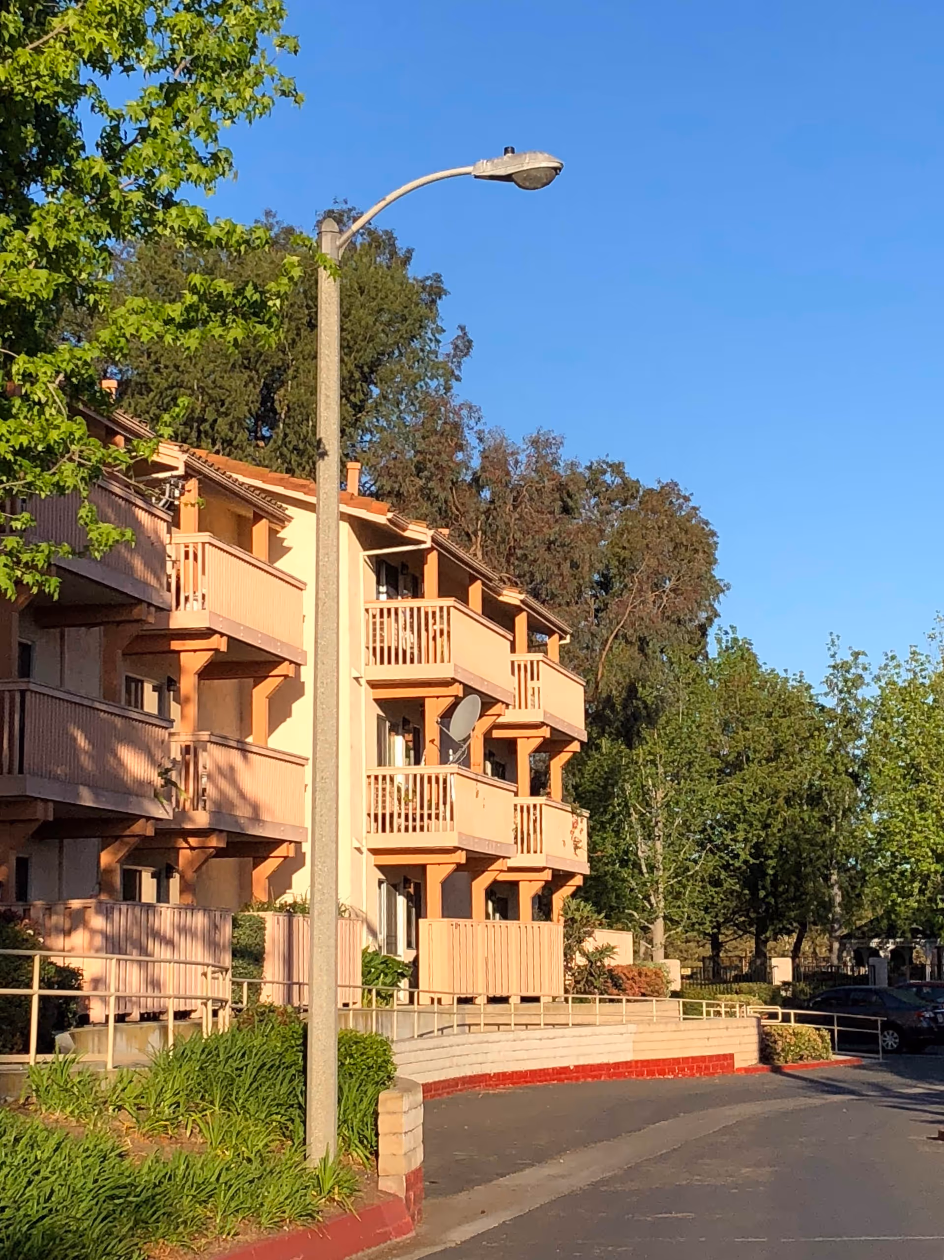 Peach-colored, multi-story senior living building with balconies, trees, and parked cars along a street.