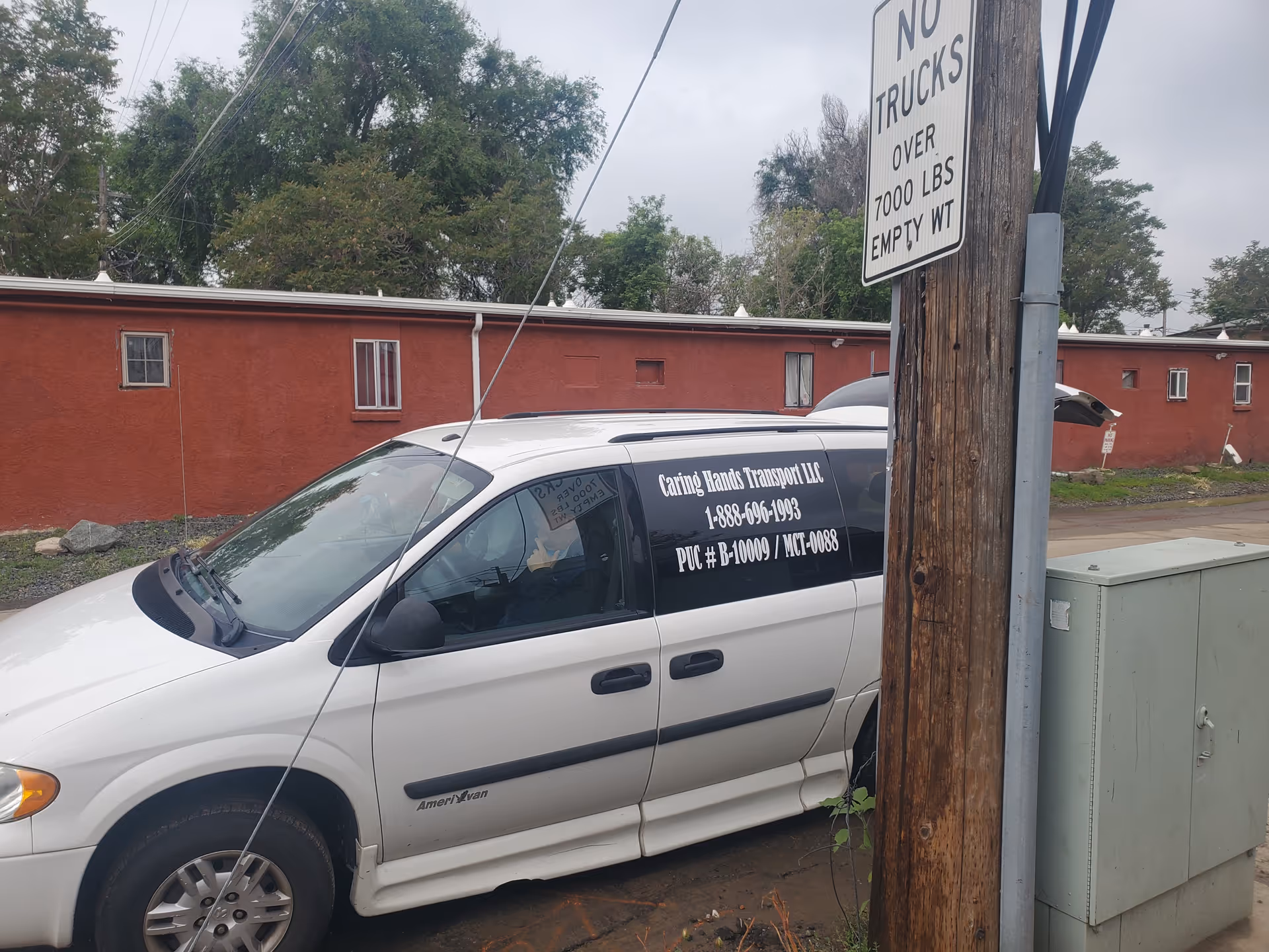 White Caring Hands Transport van parked beside a red building and utility pole.