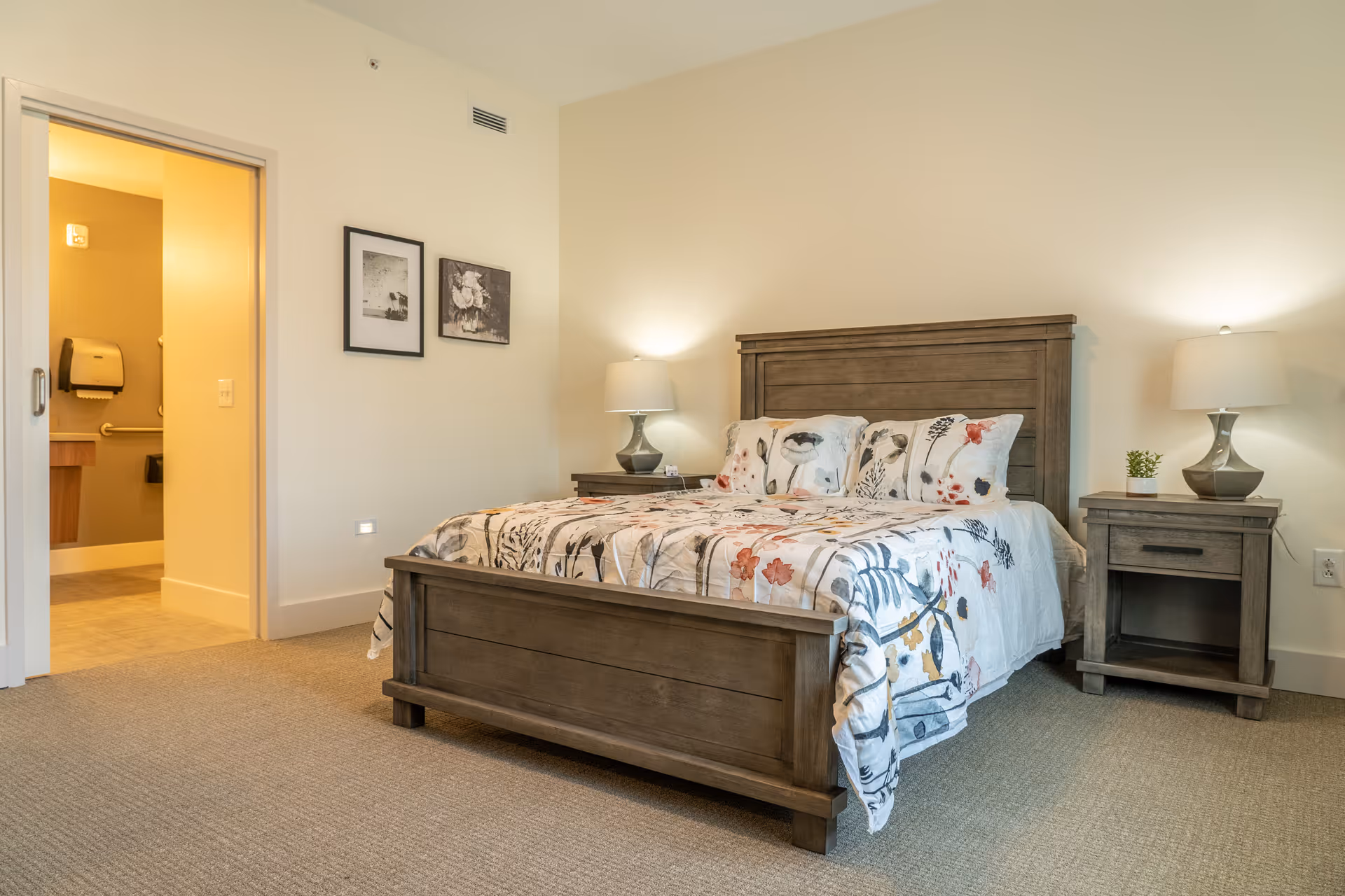 A furnished senior living bedroom featuring a wooden bed, two nightstands, and lamps.