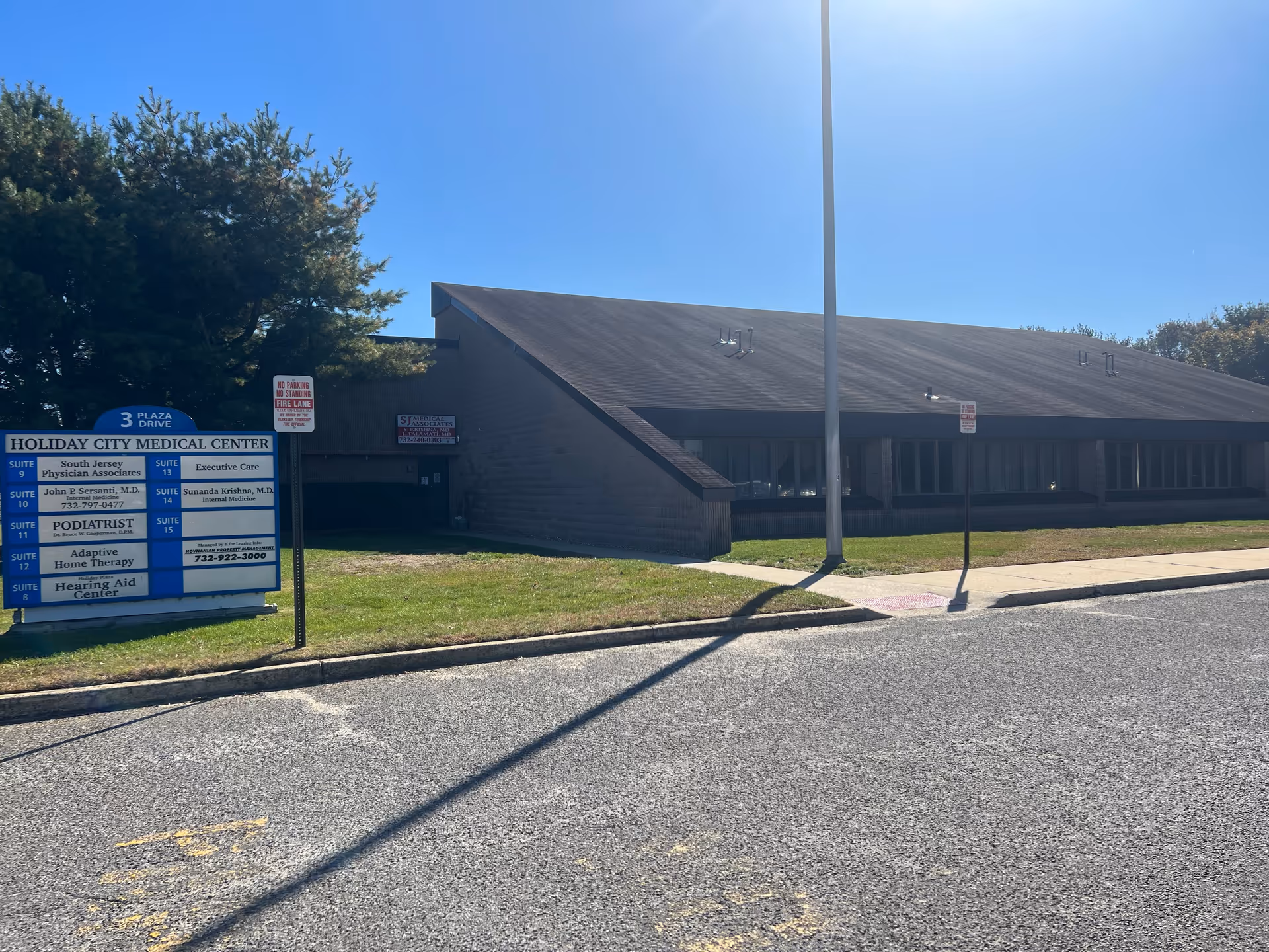 Exterior view of a low, brown-roofed building with a sign and parking area.