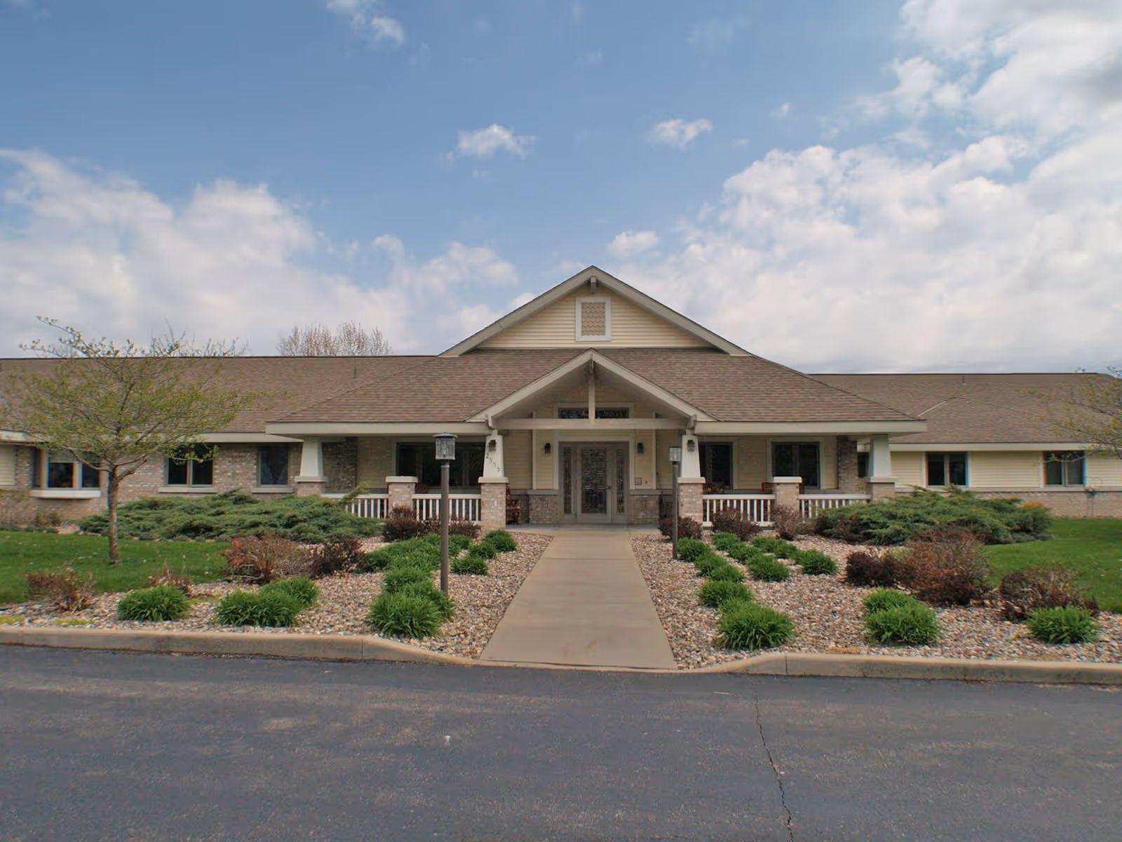 Single-story senior living facility entrance with landscaping and a paved walkway.