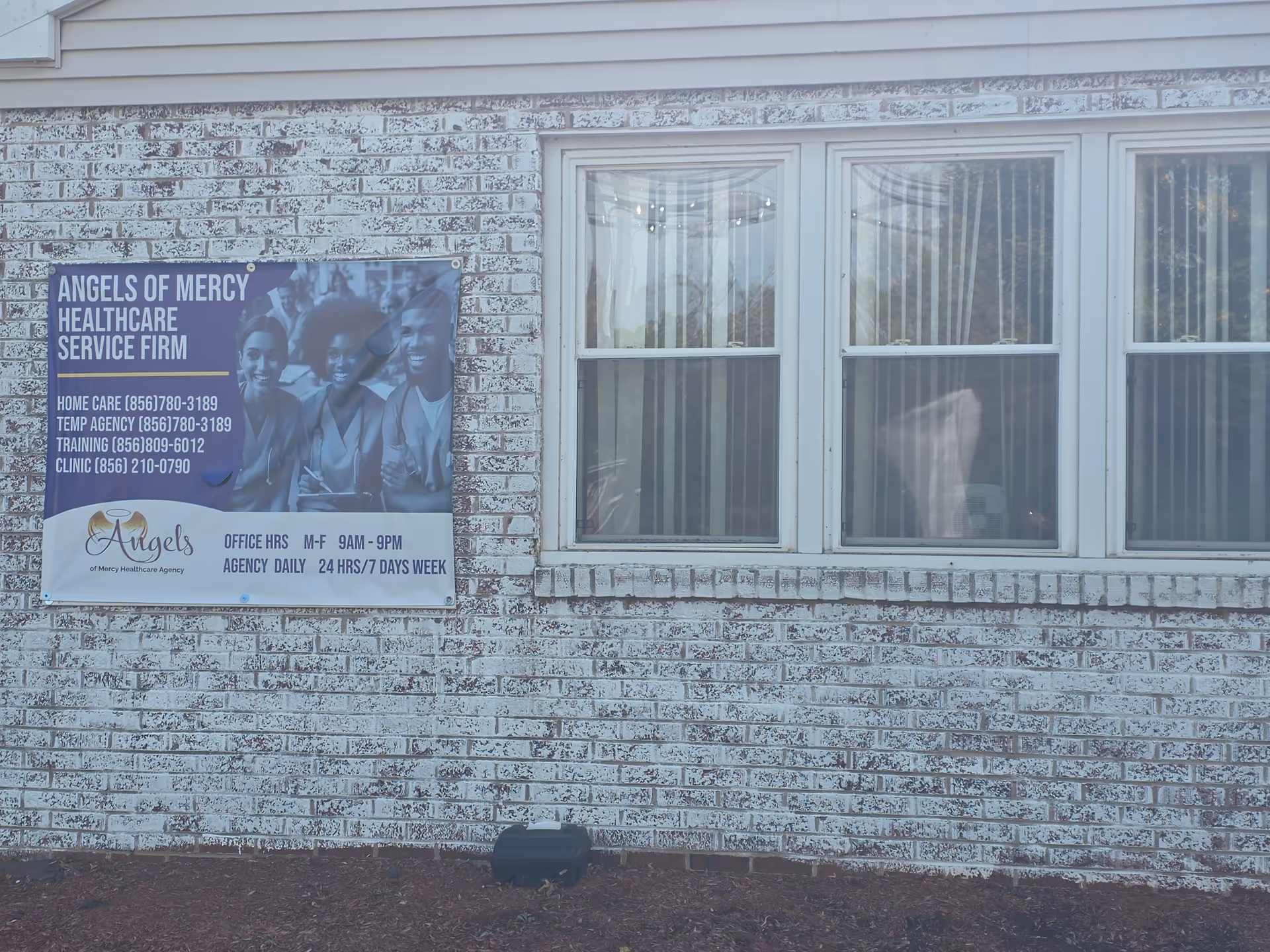 Brick exterior wall with a blue Angels of Mercy banner beside three windows.