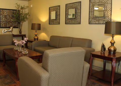 Cozy senior living center lounge with sofa set, armchairs, lamps, and wall mirrors.