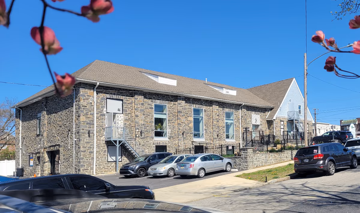 Stone-built senior living facility exterior with parked cars beside the curb.