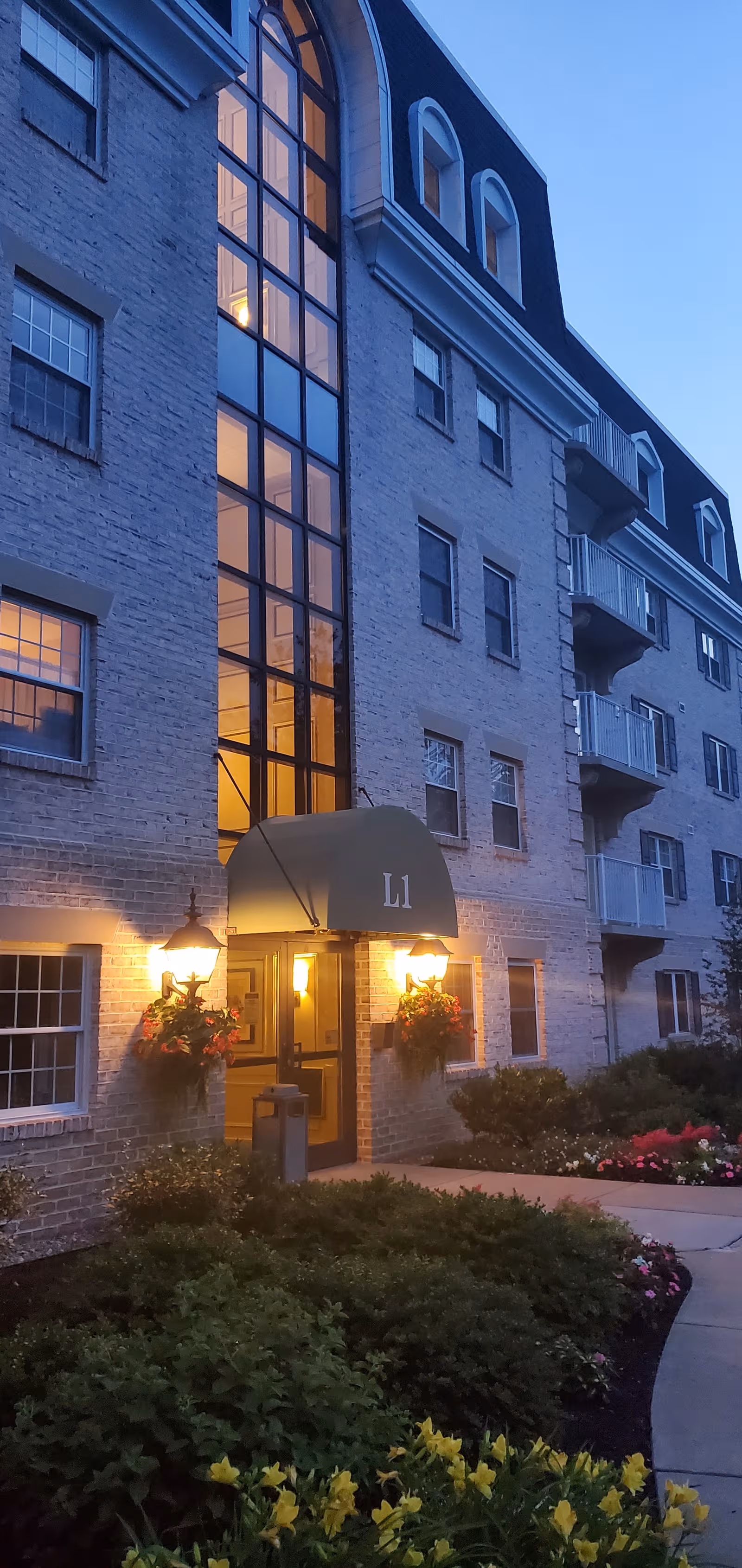 Exterior view of a multi-story senior living building with lit entrance and landscaped frontage.