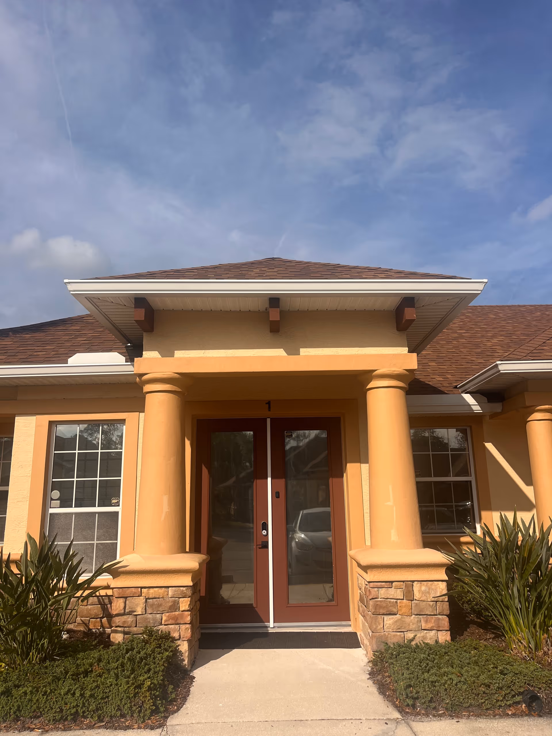 Peach-colored facility entrance with rounded columns, glass doors, and landscaped walkway.